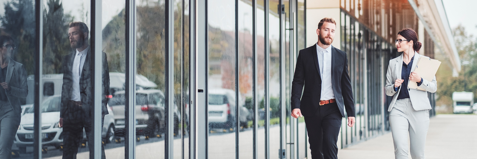 Two professionals talk while walking outside of an office building.