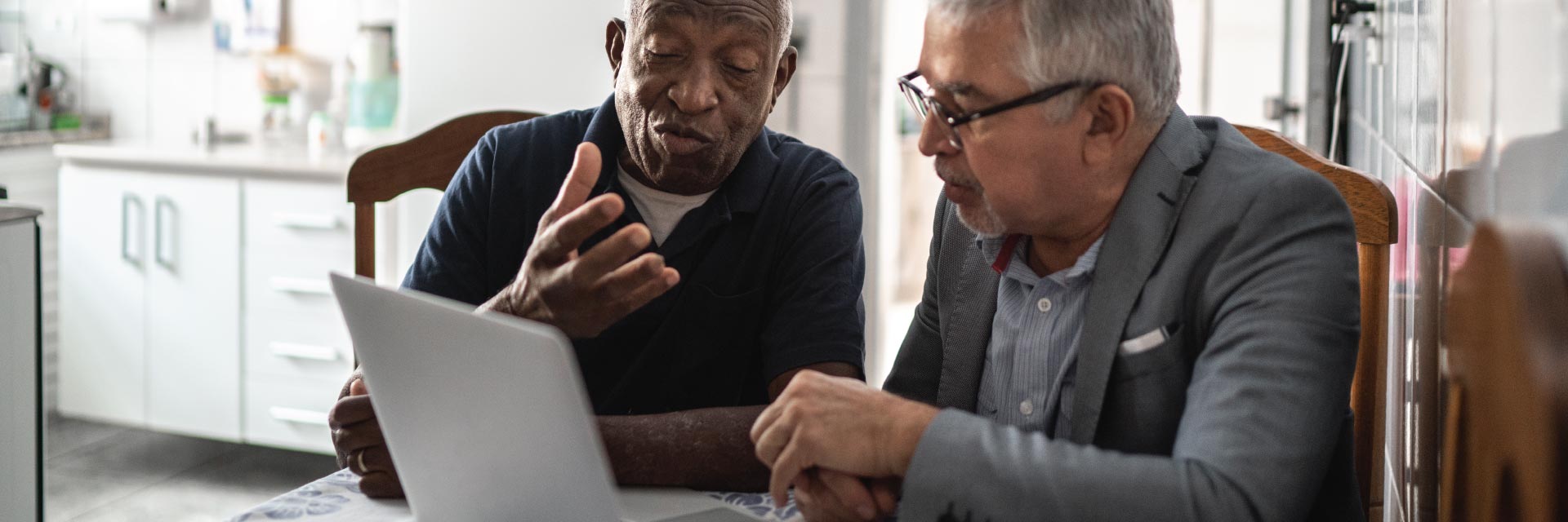 Two men talk while looking at a laptop.